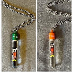 May include: Two silver chains with clear glass pendants featuring a cartoon Mickey Mouse. The pendants have a black and white image of Mickey Mouse and the text "WALT PRODUCTIONS" on the top. One pendant has a green top and the other has an orange top.
