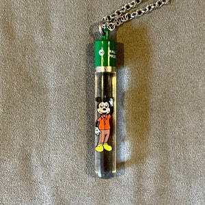 May include: A silver chain necklace with a green and silver pendant featuring a cartoon image of Mickey Mouse inside a clear tube. The tube has the text "Walt Disney World" on it.