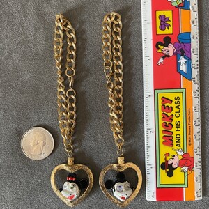 May include: Two gold chains with heart-shaped pendants featuring Mickey Mouse and Minnie Mouse. The pendants are enamel painted with black, white, and red details.