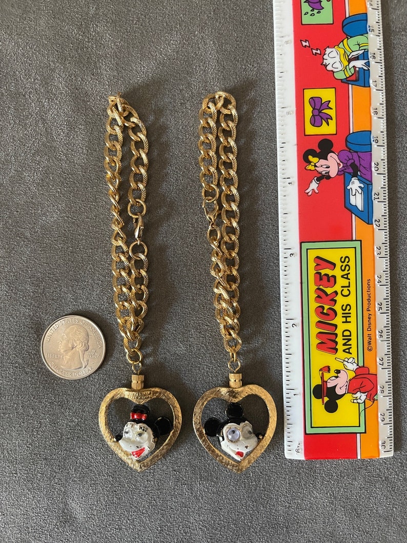 May include: Two gold chains with heart-shaped pendants featuring Mickey Mouse and Minnie Mouse. The pendants are enamel painted with black, white, and red details.