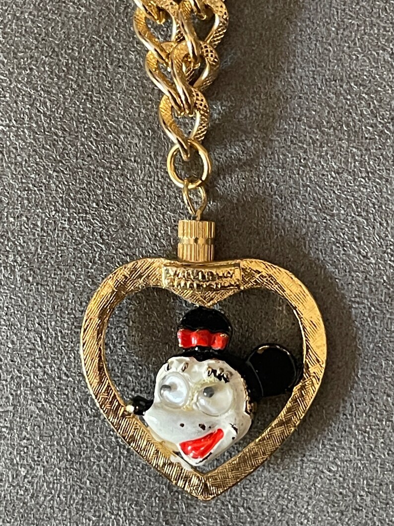 May include: Gold-tone chain necklace with a heart-shaped pendant featuring a cartoon image of Minnie Mouse. The pendant has a textured surface and the text "Walt Disney Productions" is visible on the back.