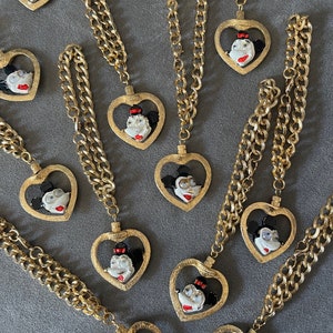 May include: A set of ten gold chain necklaces with heart-shaped pendants featuring a cartoon character with black eyes, red lips, and a black bow. Each pendant is surrounded by a gold heart frame.