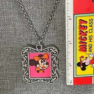 May include: Silver chain necklace with a silver picture frame pendant featuring a cartoon image of Minnie Mouse with a red bow and a pink background.