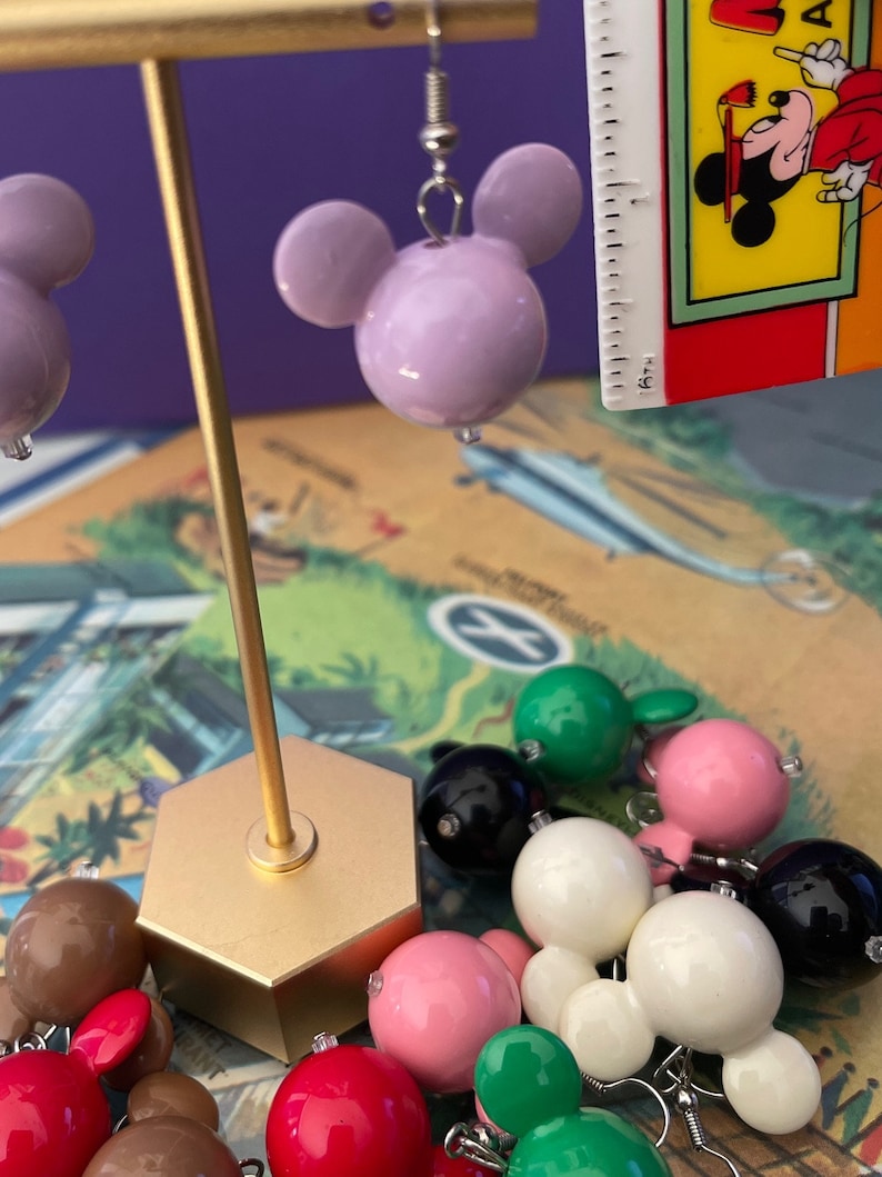 Puede incluir: Un conjunto de pendientes de Mickey Mouse de colores vivos. Los pendientes est&aacute;n hechos de pl&aacute;stico y tienen un acabado brillante. Los pendientes se muestran en un soporte dorado. Los pendientes son de varios colores, incluyendo rosa, verde, blanco, rojo y negro.