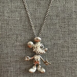 May include: Silver-coloured Mickey Mouse pendant necklace. The pendant features a detailed figure of Mickey Mouse, with sparkling crystal accents on the face. The necklace has a delicate chain and a lobster clasp.