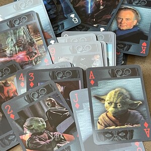 May include: A deck of playing cards featuring characters and scenes from the Star Wars franchise. The cards are blue and gray with a silver foil finish. The cards feature images of Yoda, Obi-Wan Kenobi, and other characters from the Star Wars universe.