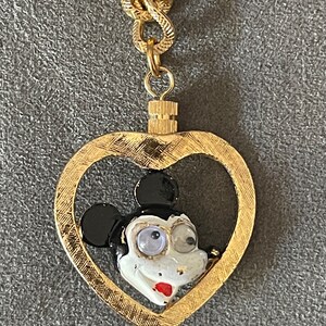 May include: A gold chain necklace with a heart-shaped pendant featuring a cartoon Mickey Mouse face with black ears, white face, and black eyes.