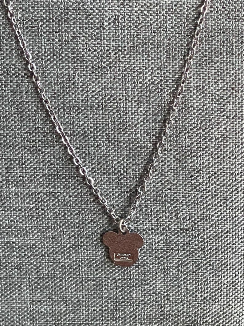 Pode incluir: Colar prateado com um pequeno pingente em forma de Mickey Mouse. O pingente &eacute; de cor s&oacute;lida e tem uma argola para a corrente. A corrente &eacute; feita de pequenos c&iacute;rculos ligados.