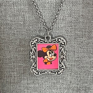 May include: A silver chain necklace with a silver picture frame pendant featuring a cartoon image of Minnie Mouse with a pink background.