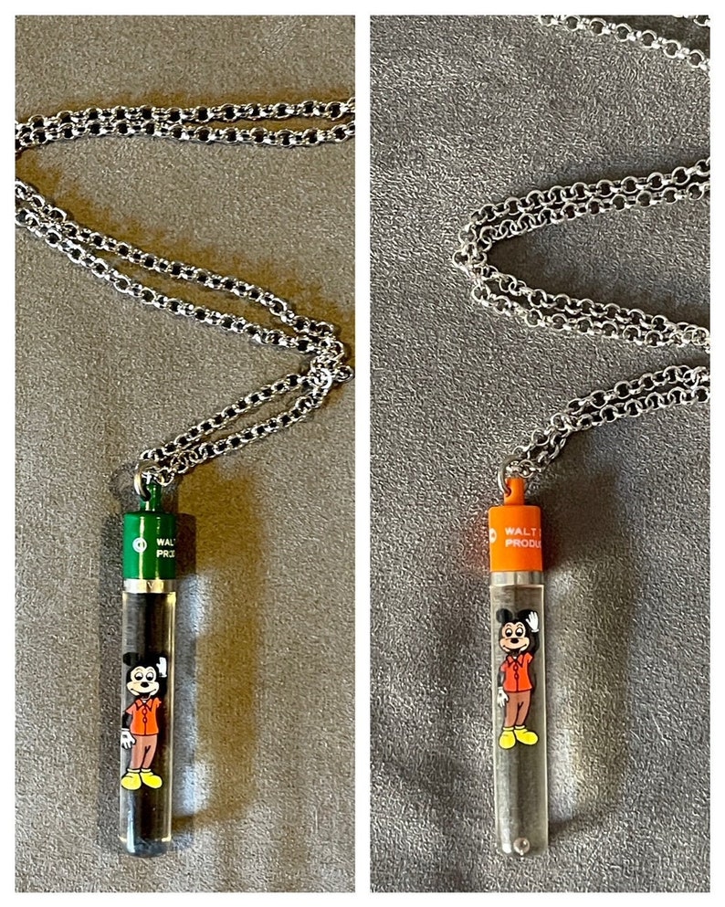 May include: Two silver chains with clear glass pendants featuring a cartoon Mickey Mouse. The pendants have a black and white image of Mickey Mouse and the text "WALT PRODUCTIONS" on the top. One pendant has a green top and the other has an orange top.