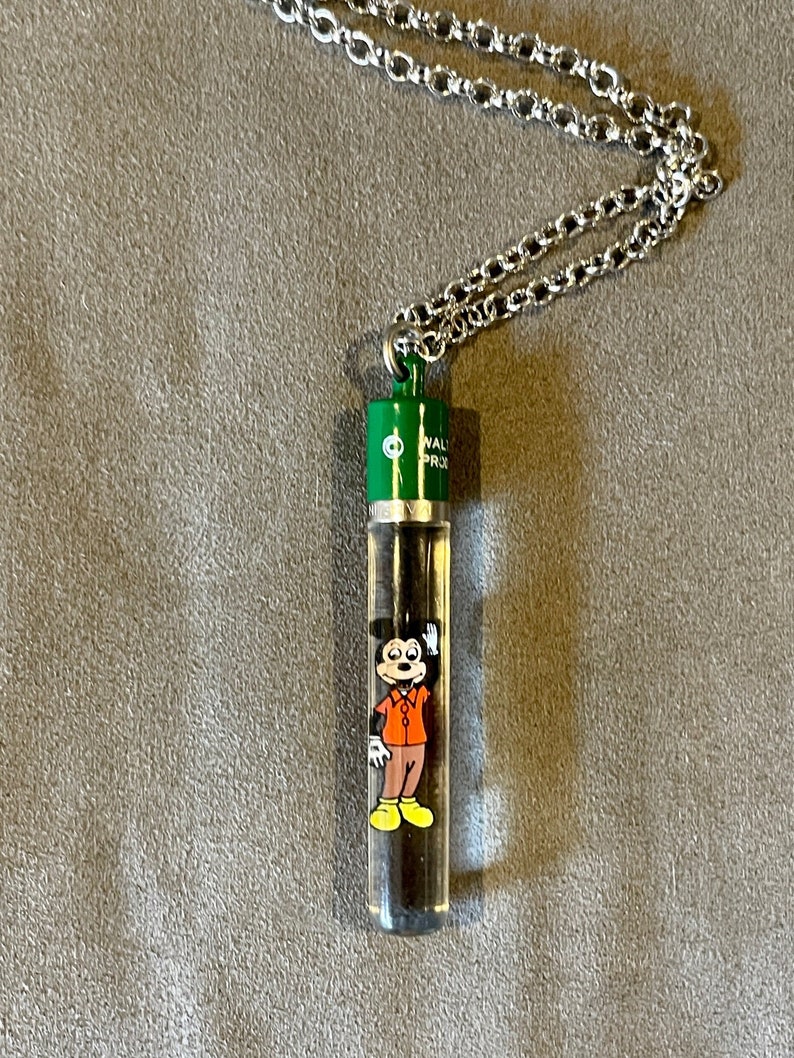 May include: A silver chain necklace with a green and silver pendant featuring a cartoon image of Mickey Mouse inside a clear tube. The tube has the text "Walt Disney World" on it.