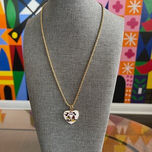 May include: A gold chain necklace with a heart-shaped pendant featuring a cartoon image of Mickey Mouse and Minnie Mouse kissing.