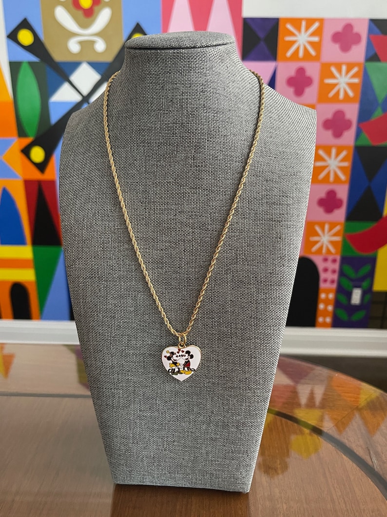 May include: A gold chain necklace with a heart-shaped pendant featuring a cartoon image of Mickey Mouse and Minnie Mouse kissing.