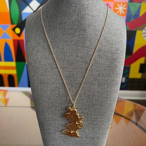 May include: A gold necklace with a pendant shaped like a cartoon mouse. The pendant is detailed and has a textured surface.