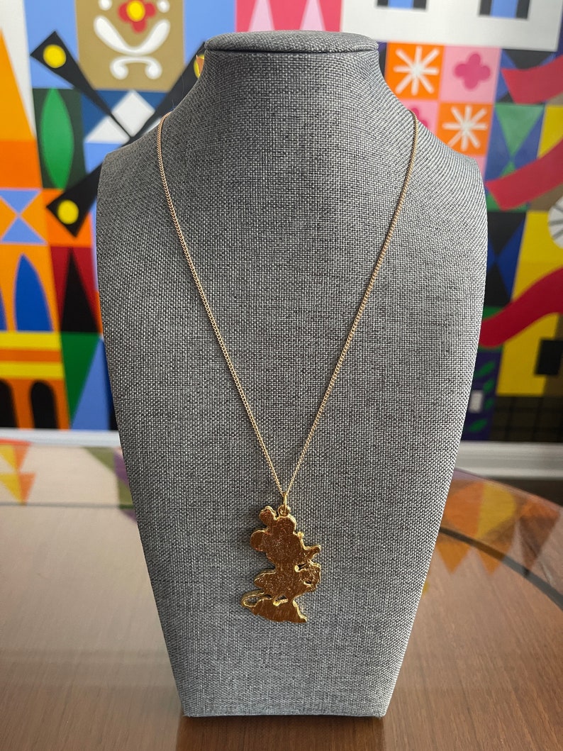 May include: A gold necklace with a pendant shaped like a cartoon mouse. The pendant is detailed and has a textured surface.