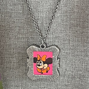May include: A silver chain necklace with a silver frame pendant featuring a cartoon image of Minnie Mouse with a pink background and orange bow.