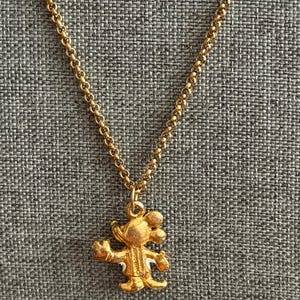 K&ouml;nnte beinhalten: Eine goldfarbene Halskette mit einem Anh&auml;nger in Form einer Zeichentrickmaus. Der Anh&auml;nger hat ausgestreckte Arme und ein l&auml;chelndes Gesicht. Die Kette ist zart goldfarben.