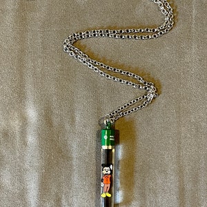 May include: A silver chain necklace with a green and clear glass pendant featuring a cartoon image of Mickey Mouse. The pendant says "Walt Disney" on the side.