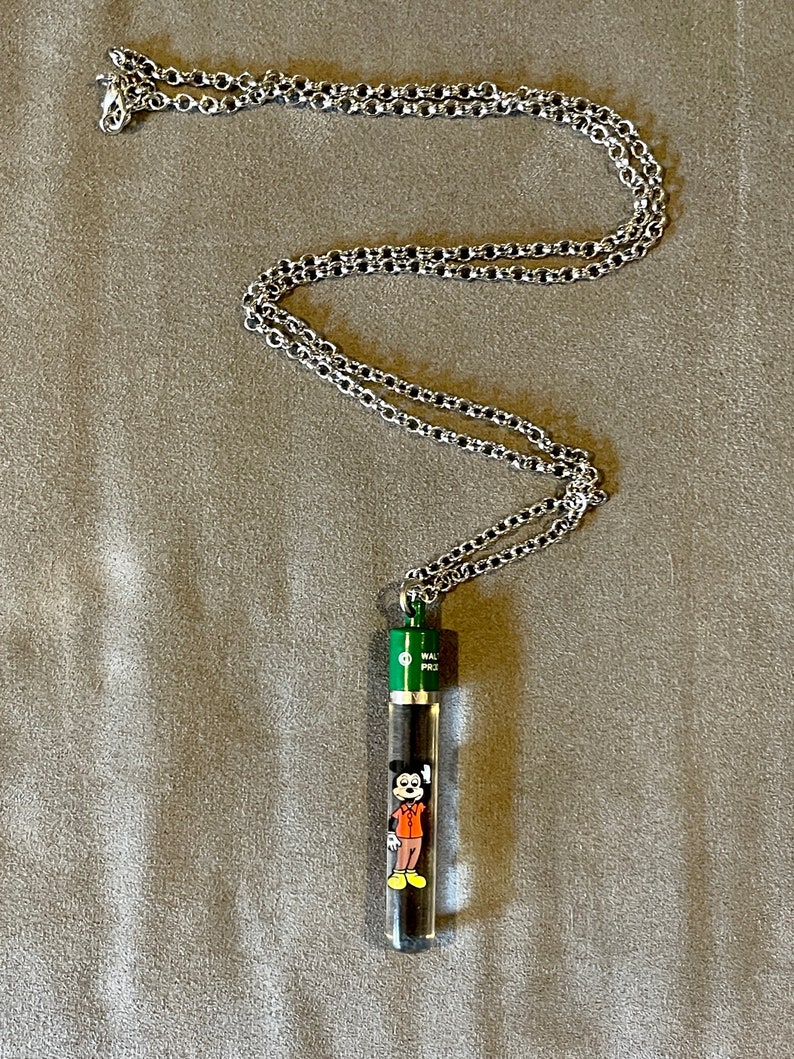 May include: A silver chain necklace with a green and clear glass pendant featuring a cartoon image of Mickey Mouse. The pendant says "Walt Disney" on the side.