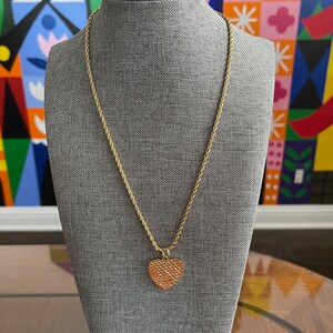 May include: A gold chain necklace with a textured heart pendant. The necklace is displayed on a gray mannequin.