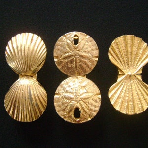 May include: Three gold-colored metal ornaments shaped like seashells and sand dollars. The seashells are open and the sand dollars have a five-pointed star design.