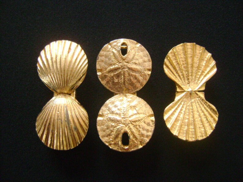 May include: Three gold-colored metal ornaments shaped like seashells and sand dollars. The seashells are open and the sand dollars have a five-pointed star design.