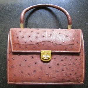 May include: A brown ostrich leather handbag with a gold clasp and handle.