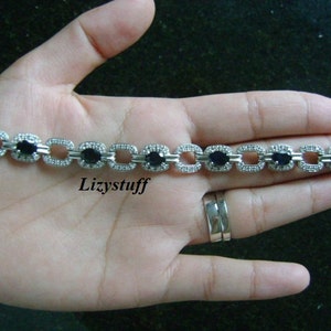May include: A silver bracelet with a chain link design and black oval-shaped stones set in each link. The bracelet is on a person's hand.