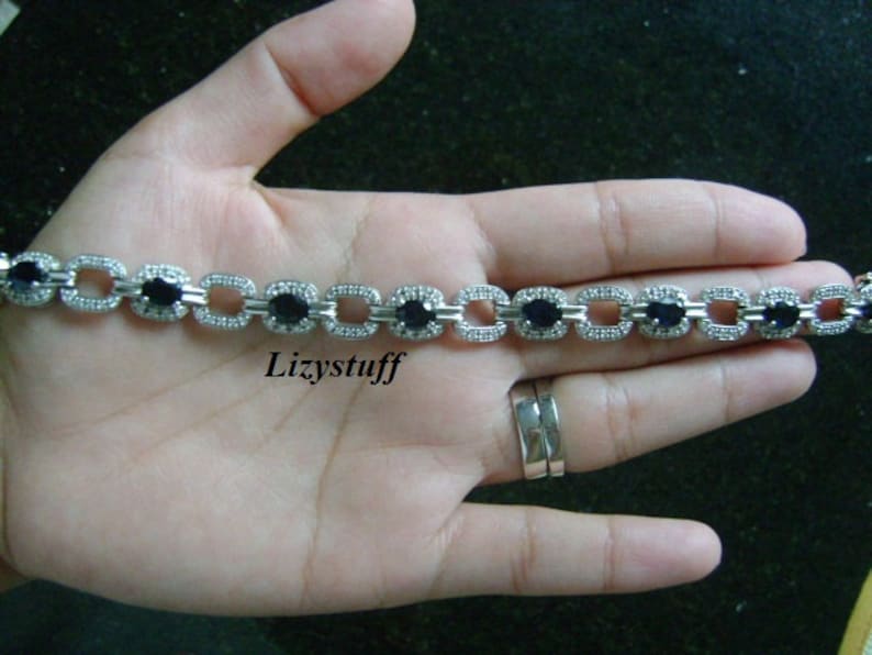 May include: A silver bracelet with a chain link design and black oval-shaped stones set in each link. The bracelet is on a person's hand.