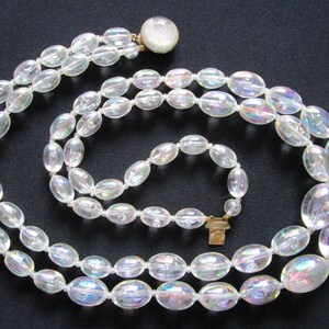 May include: A double strand iridescent glass bead necklace with a gold clasp. The beads are oval shaped and have a pearlescent finish.