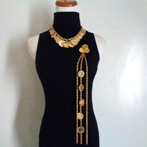 May include: A gold-tone necklace and matching brooch with a chain and coin design. The necklace is layered and the brooch hangs from a long chain.