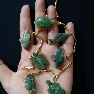 May include: A gold chain necklace with green jade animal charms. The charms include a turtle, fish, elephant, and more.