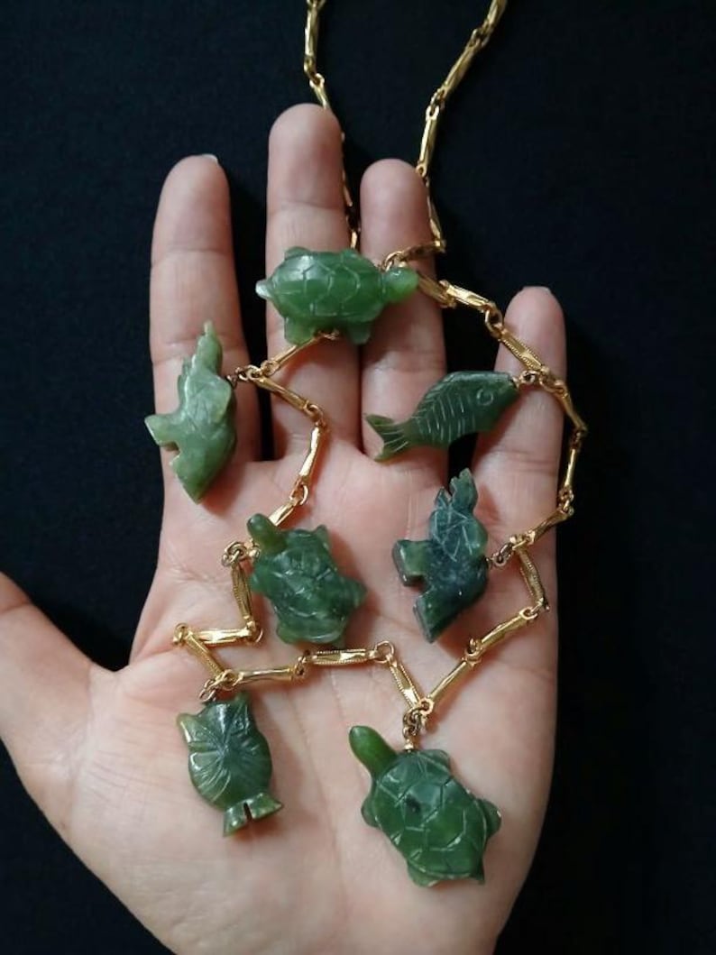 May include: A gold chain necklace with green jade animal charms. The charms include a turtle, fish, elephant, and more.