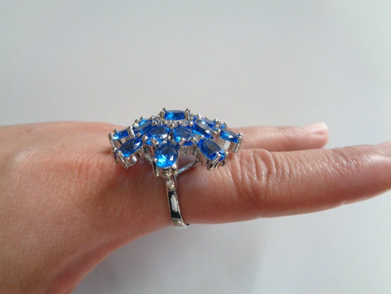 May include: A silver ring with a cluster of blue oval-shaped gemstones. The ring is set on a finger.