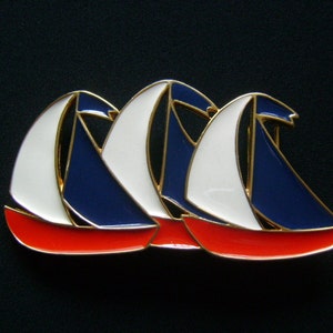 May include: Three sailboats in a row, each with a red, white, and blue design. The sailboats are made of metal and have a gold finish.