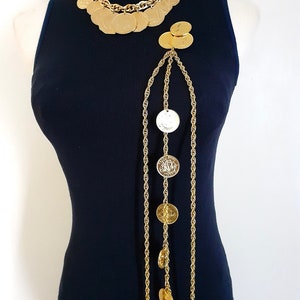 May include: A gold chain necklace with multiple large round coin-shaped pendants. The necklace is layered and has a long, dangling chain with additional coin-shaped pendants.