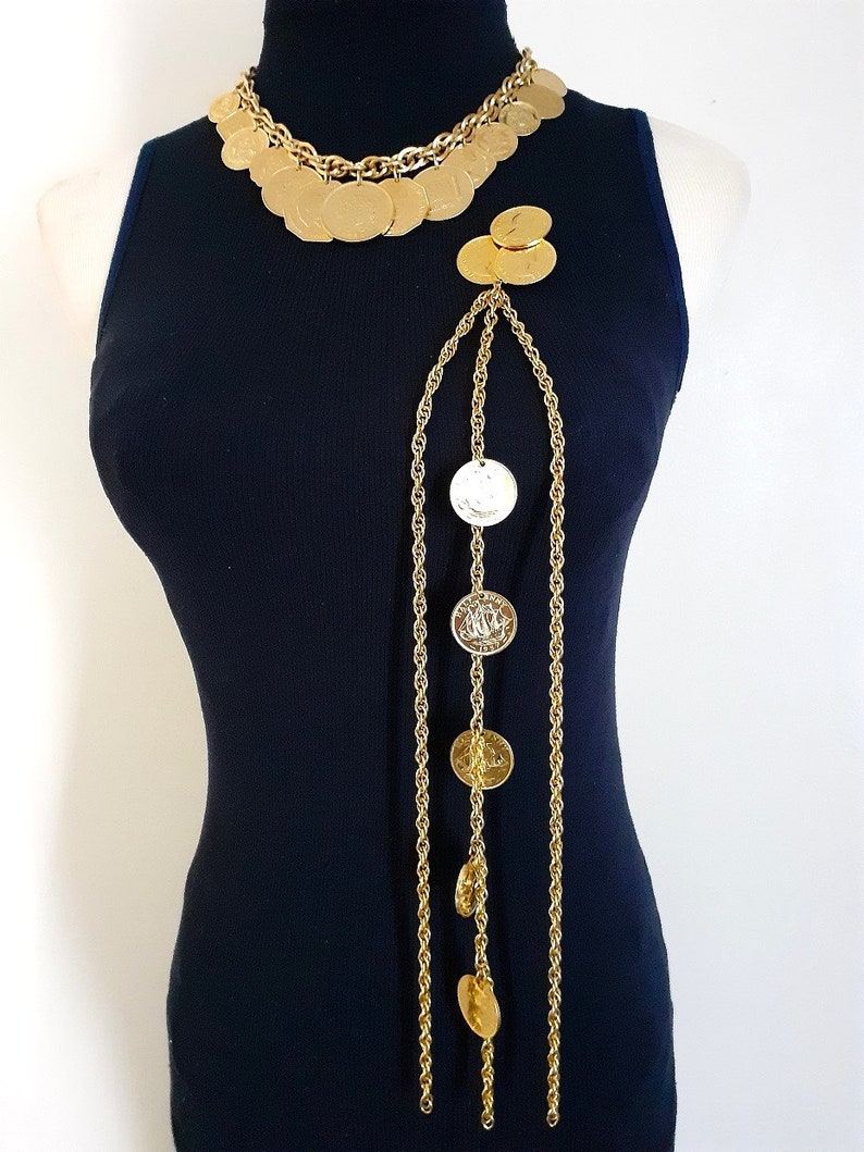 May include: A gold chain necklace with multiple large round coin-shaped pendants. The necklace is layered and has a long, dangling chain with additional coin-shaped pendants.