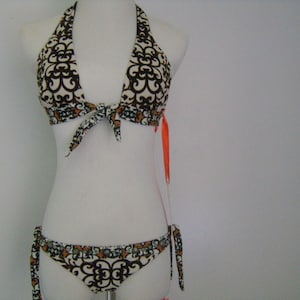 May include: A brown and white patterned bikini top and bottom with orange ties. The top is a halter style with a tie in the front. The bottom has a low rise and ties on the sides.