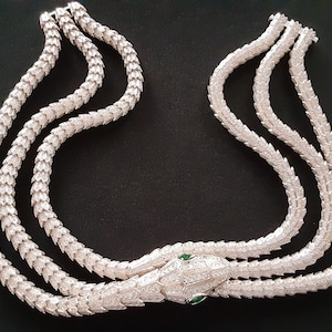 Peut inclure: Un collier de serpent en argent avec une t&ecirc;te de serpent incrust&eacute;e de diamants et des yeux verts. Le collier est compos&eacute; de trois rangs d'&eacute;cailles de serpent.