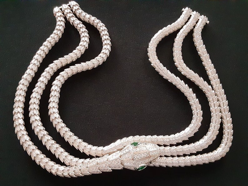 Peut inclure: Un collier de serpent en argent avec une t&ecirc;te de serpent incrust&eacute;e de diamants et des yeux verts. Le collier est compos&eacute; de trois rangs d'&eacute;cailles de serpent.