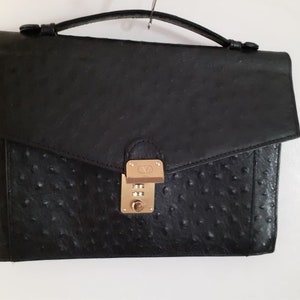 May include: A black leather briefcase with a gold combination lock. The briefcase has a textured, ostrich-like pattern.