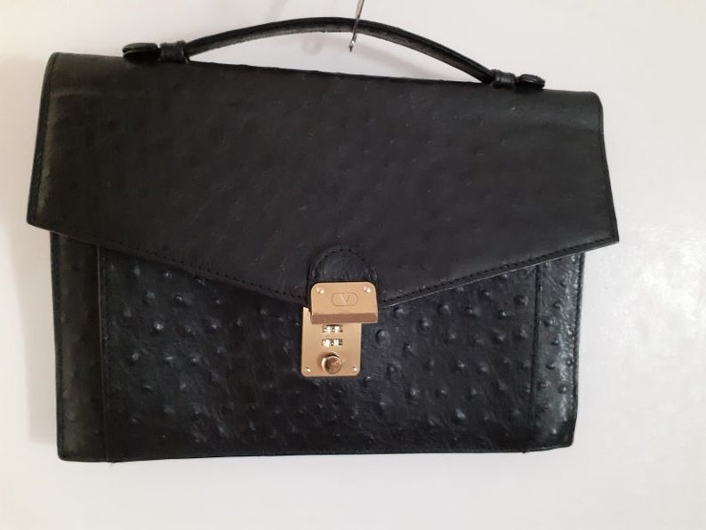 May include: A black leather briefcase with a gold combination lock. The briefcase has a textured, ostrich-like pattern.