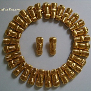 May include: A gold-tone necklace and matching earrings. The necklace is made of a series of linked, textured, cylindrical beads. The earrings are simple, with a single textured, cylindrical bead.