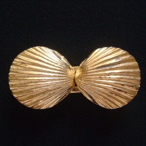 May include: A gold-tone metal seashell-shaped belt buckle. The buckle is made of two halves that are hinged together.