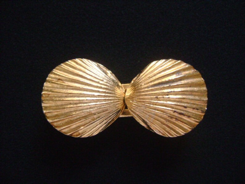 May include: A gold-tone metal seashell-shaped belt buckle. The buckle is made of two halves that are hinged together.