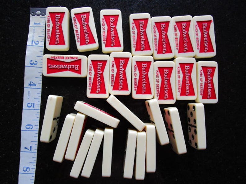 May include: A set of dominoes with a Budweiser King of Beers theme. The dominoes are white with black dots and feature a red and white Budweiser logo.