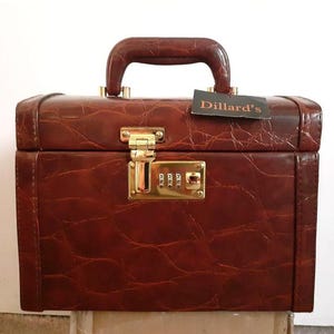 May include: A brown leather Dillard's travel case with a combination lock and a gold metal handle.