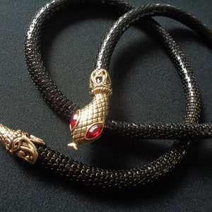 May include: A black snake chain necklace with a gold snake head pendant featuring red gemstone eyes.