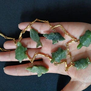 May include: A gold chain necklace with green jade pendants shaped like fish and turtles.