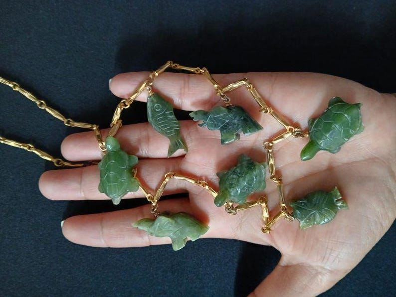 May include: A gold chain necklace with green jade pendants shaped like fish and turtles.